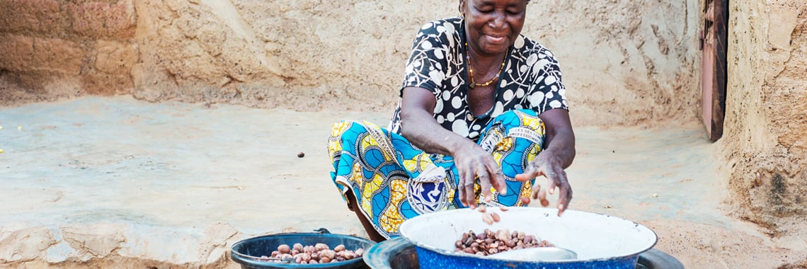 Image showing a female farmer working stitting down with a bowl of Shea Nuts courtesy of AAK and Kolo Nafaso for Shedid & Parrish